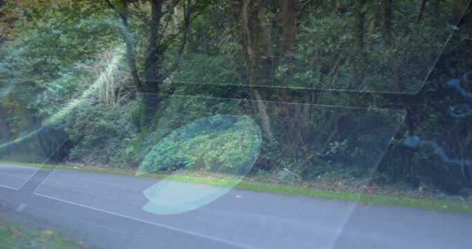 Vehicle moving forward left causing reflections shifting, revealing road, trees, and autumn leaves