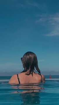 Caucasian Woman In Infinity Pool Smiling Over Turquoise Sea Horizon, Sunglasses On, Head Bobbing Above Calm Water, Joyful Morning Swim, Travel Influencer And Adventurer Vibe, Closeup Reflections