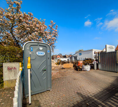 G&uuml;tersloh,Deutschland -01.04.2026: DIXI Mobile Toiletten Kabine auf einer Baustelle,idylisch unter einem bl&uuml;henden Magnolienbaum neben einer Baustellenabsperrung