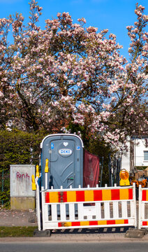 G&uuml;tersloh,Deutschland -01.04.2026: DIXI Mobile Toiletten Kabine auf einer Baustelle,idylisch unter einem bl&uuml;henden Magnolienbaum neben einer Baustellenabsperrung