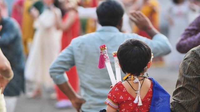 Child celebrating Ganesh Chaturthi festival, holding dandiya sticks and dancing in crowd
