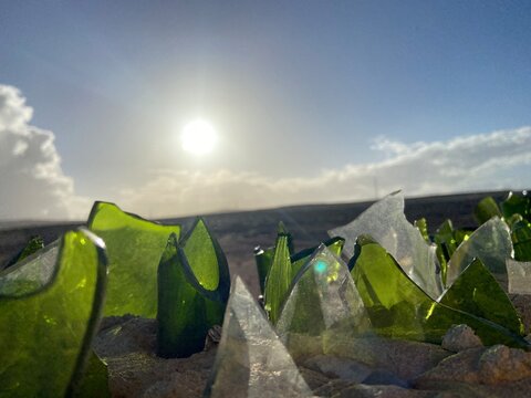 Close-up of broken green clear glass shards embedded in the top of a concrete wall as a traditional security barrier. Dramatic low-angle view, blue sky and clouds, suitable for concepts of security