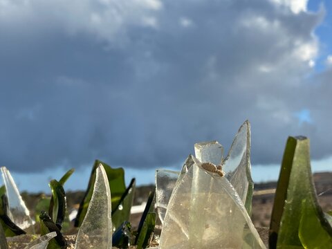 Close-up of broken green clear glass shards embedded in the top of a concrete wall as a traditional security barrier. Dramatic low-angle view blue sky and clouds, suitable for concepts of security