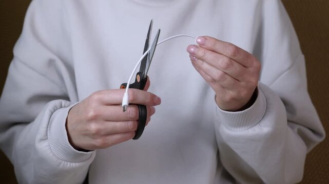 Woman cutting broken usb cable with scissors. Frustrated woman's hands cutting a white broken usb charging cable in half with scissors, symbolizing digital detox, planned obsolescence