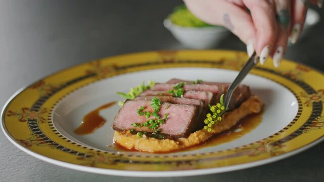 Sliced NY strip steak with sweet potato mash, demi glace and herb garnish on a decorative plate.