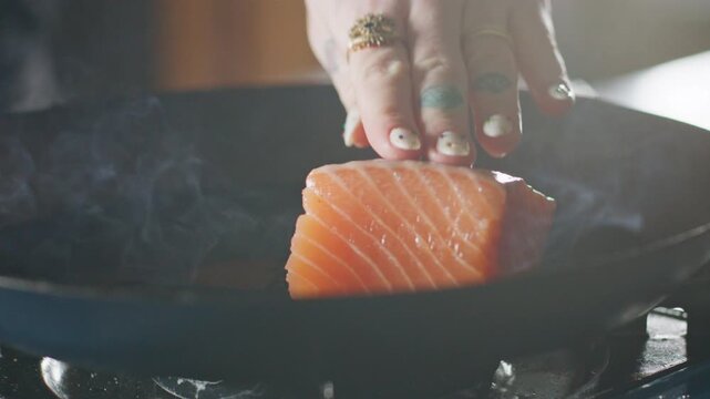 Salmon fillets placed in a hot pan, sizzling on the stovetop.