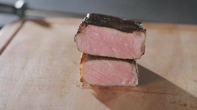 Two stacked slices of medium-rare NY strip wait to be sliced on a wooden cutting board.