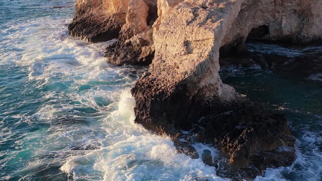 Aerial drone view of the Bridge of Love, a natural rock arch formation in Ayia Napa, Cyprus. Turquoise waves flow beneath the limestone arch