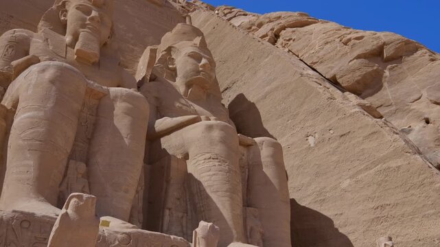 Close-up of giant Ramesses II colossi carved into rock facade at Abu Simbel temple, Egypt. Dramatic upward view of ancient sandstone pharaoh statues. Travel and history.
