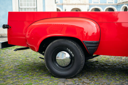Close-Up Of Red Vintage Pickup Truck Wheel Parked On Cobblestone Street With Reflective Hubcap