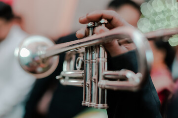 Fototapeta premium Close-up of a Musician's Hand Holding a Silver Trumpet, Ready to Play a Melodic Tune in a Blurred Background Setting