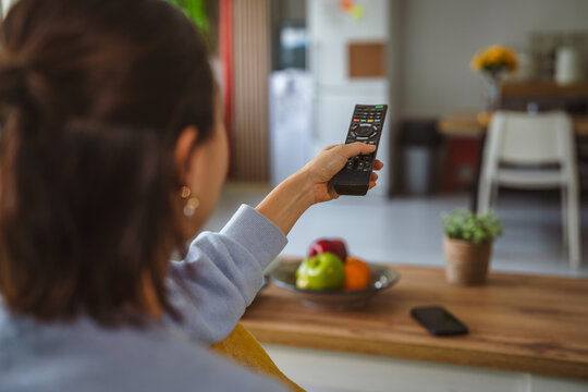 Woman holding remote control changing television channels at home