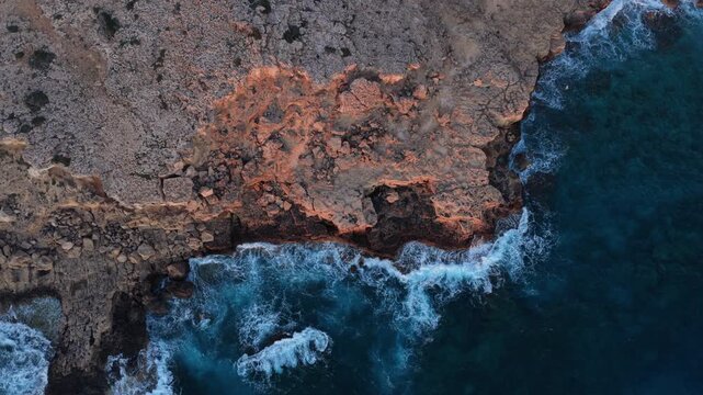 Aerial drone view of waves crashing against rocky cliffs in Cyprus, creating dynamic ocean textures