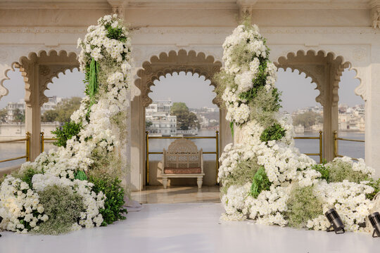 Elegant floral archway decoration for a luxurious event or wedding venue, with white flowers and green foliage, set against an ornate architectural backdrop by a serene lake