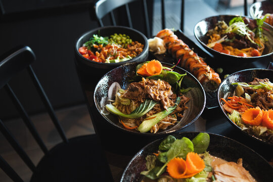 A variety of Asian dishes served in a modern restaurant setting, featuring noodles, sushi, and fresh ingredients красиво presented for dining and sharing.