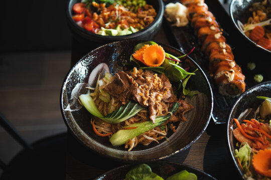 A variety of Asian dishes served in a modern restaurant setting, featuring noodles, sushi, and fresh ingredients красиво presented for dining and sharing.