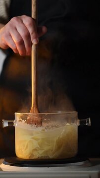A female cook boils pasta in a transparent pot on a kitchen stove, showing a clean and authentic cooking process suitable for both home and professional restaurant environments.