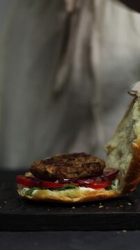 A woman prepares homemade burgers in a kitchen, cooking and assembling fresh ingredients in a process that reflects both home kitchen and professional restaurant-style cooking.