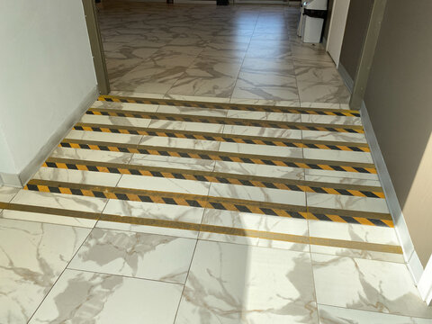 Beveled floor transition marked with black-and-yellow hazard striping. There is a slight level difference between two areas.