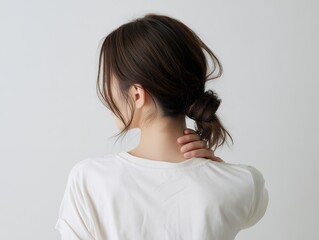 Fototapeta premium 首の痛みや肩こりに悩み手を添える後ろ姿の女性と清潔感のある白いTシャツのライフスタイル