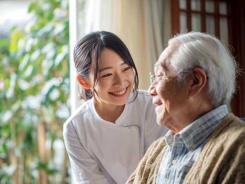 明るい室内で笑顔の介護士の女性にケアされながら穏やかに微笑む高齢者男性の接写写真