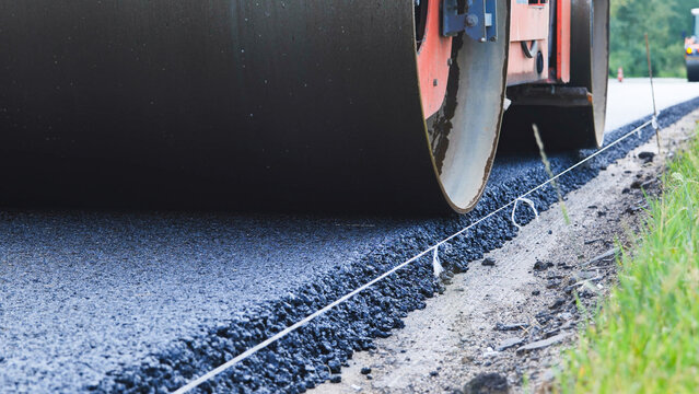 Road roller compacting fresh asphalt on a new road construction site