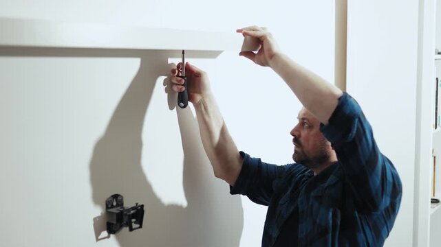 Close up of man screwing bolt into wall shelf with manual screwdriver, DIY home repair, 4K.
