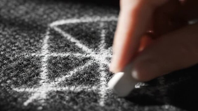 Close-up of a hand drawing a geometric pattern with chalk on a dark, textured surface, creating a mesmerizing visual effect.