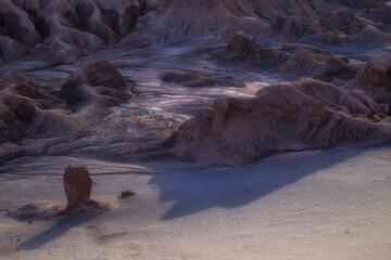 Fototapeta premium A high-angle view of rugged rock formations and salt-encrusted craters in the Atacama Desert. The dramatic sunset lighting creates deep shadows across the barren, alien-like terrain. 