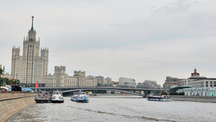 Fototapeta premium Moscow city skyline with Stalinist skyscraper and river traffic under a cloudy sky