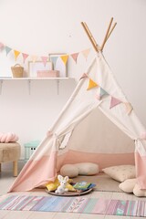 Cute wigwam with pillows, books and toys in stylish child's room © New Africa