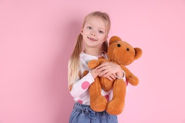 Little girl hugging her teddy bear on pink background