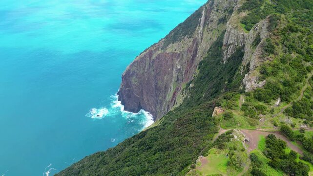 Dramatic aerial view of Madeira's eastern coastline, where lush green cliffs meet the vibrant turquoise Atlantic, showcasing the island's wild, untamed beauty. Vereda do Larano