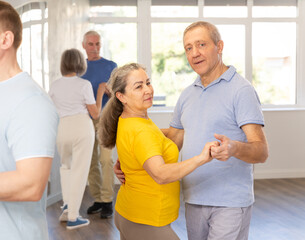 Fototapeta premium Happy smiling elderly woman enjoying impassioned merengue with male partner in latin dance class. Social dancing concept..