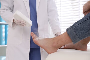 Obraz premium Doctor applying talcum powder onto man's foot in clinic, closeup