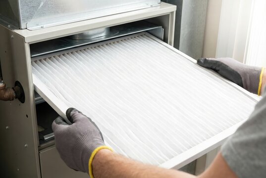 Technician wearing gloves sliding a new clean white air filter into an HVAC furnace