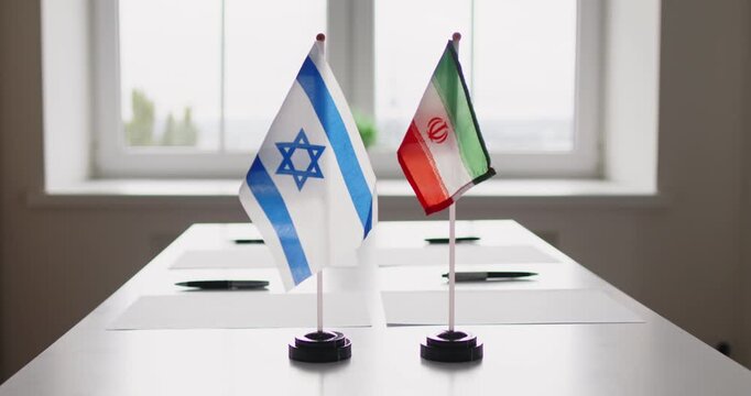 Diplomacy negotiation flags at meeting table talks. Israeli and Iranian desk flags face across a meeting table, implying bilateral dialogue and cautious mediation. Peace talks symbol on table.