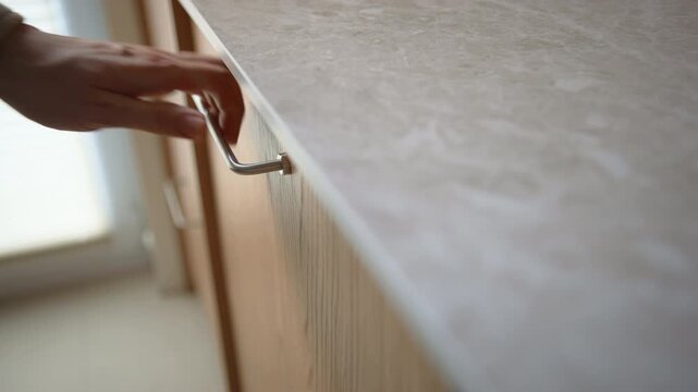 Man closing dishwasher door in modern kitchen. Wooden cabinets, organized tableware and home interior details highlight everyday household routine in residential space. Daylight, close-up shot