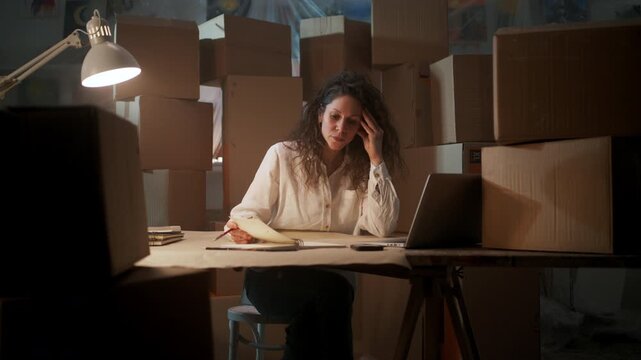 Busy Woman Working, Hardworking Woman In Dim Storage Complete With Laptop And Boxes During Late Hours