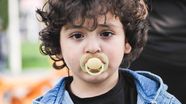 Little boy with curly hair using pacifier, looking at camera