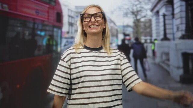 Woman smiling and pointing index finger upward on a busy city street beside a red doubledecker bus and walking pedestrians; delight curiosity wonder.