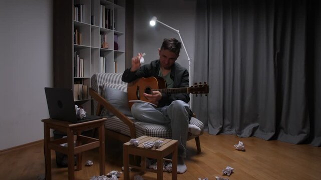 Frustrated musician crumpling sheet music while sitting with an acoustic guitar, surrounded by crumpled papers, struggling with inspiration and creative block in a home studio