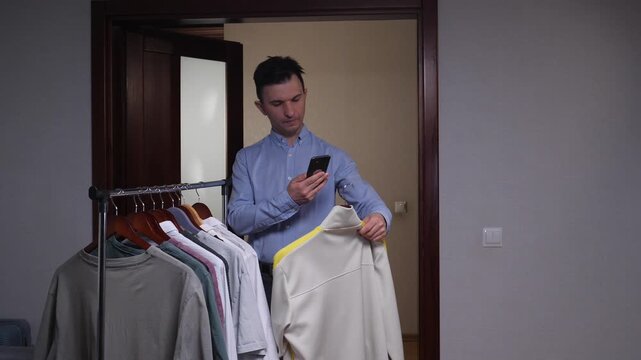 Young man photographing clothing on a rack with a smartphone, preparing apparel for online resale and e commerce listings for a small fashion business or marketplace