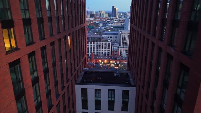 Aerial perspective looking between two modern brick high-rise buildings toward the Manchester skyline during the quiet moments of dawn.
