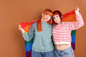 Lovely lesbian couple with rainbow flag on brown background. LGBT concept