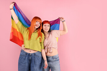 Lovely lesbian couple with rainbow flag on pink background, space for text. LGBT concept