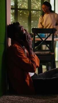 Vertical Video Young adult, African American, overwhelmed and unfulfilled, sitting on the floor at home, struggling with anxiety and mental illness concept. Man in depressive mood, solitude and sorrow