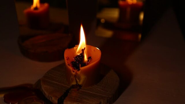A brightly burning candle against a dark background near a mirror, the candle flame dripping melted wax onto the table. A magical witch ritual.