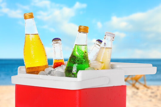 Cooler box with different drinks and ice on beach near sea