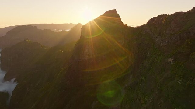 Aerial view at Pico do Arieiro of mountains over clouds with blooming Cytisus shrubs on sunset with sunburst. Madeira island, Portugal. Pull away out dolly retreat shot